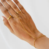 Gold hand chain worn on a hand against a light background