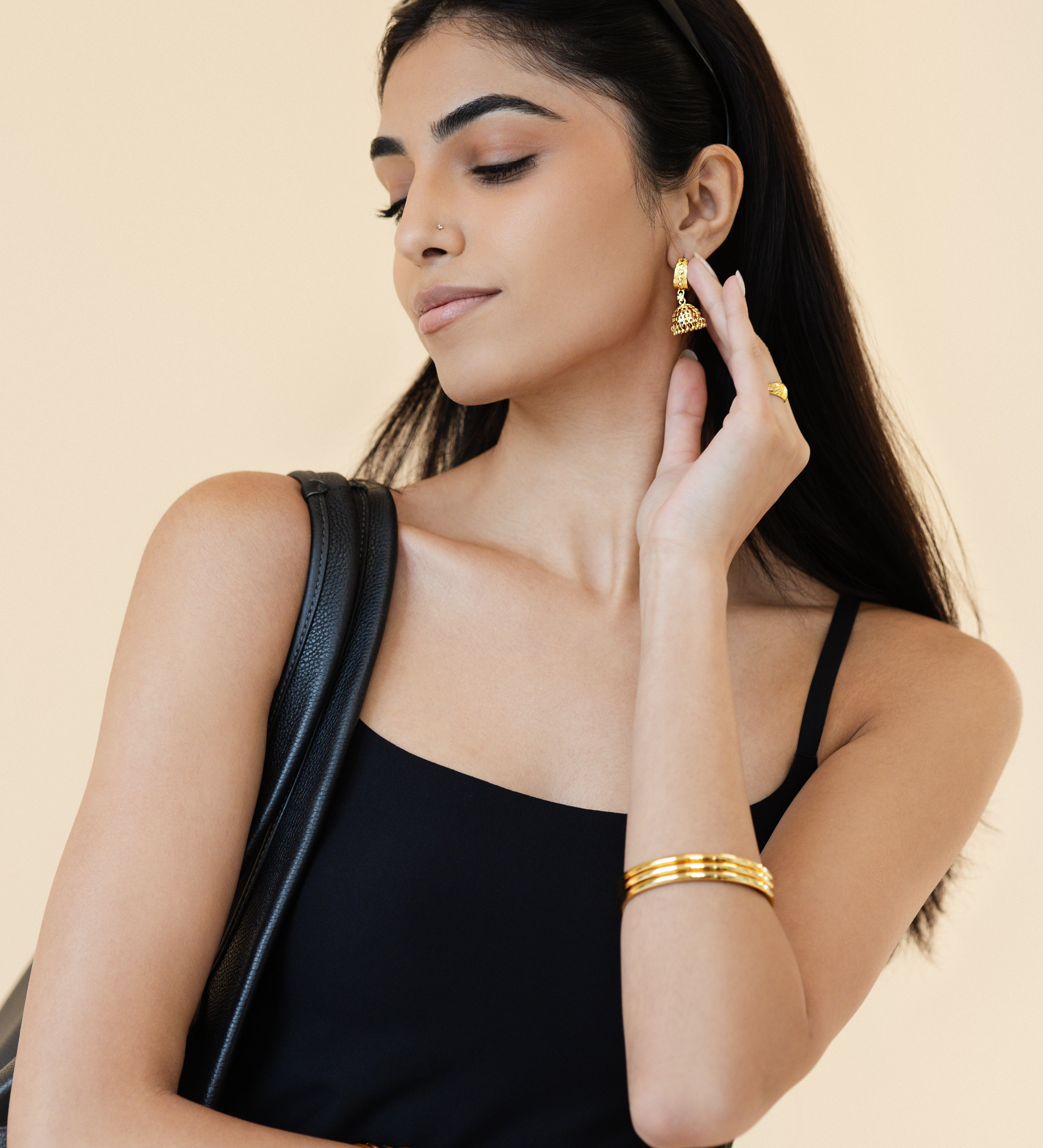 Woman wearing gold jewelry against a beige background