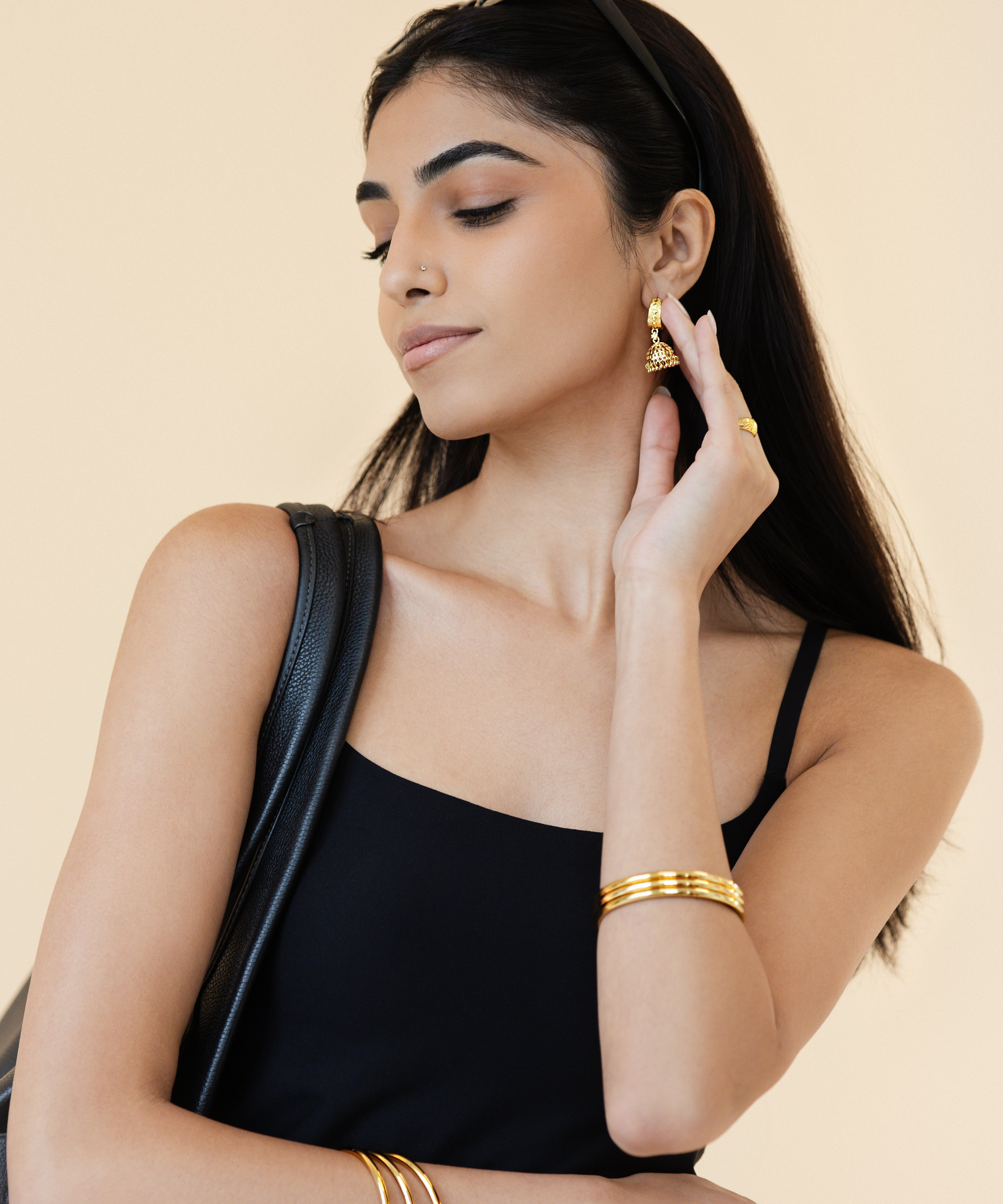 Woman wearing gold jewelry against a beige background