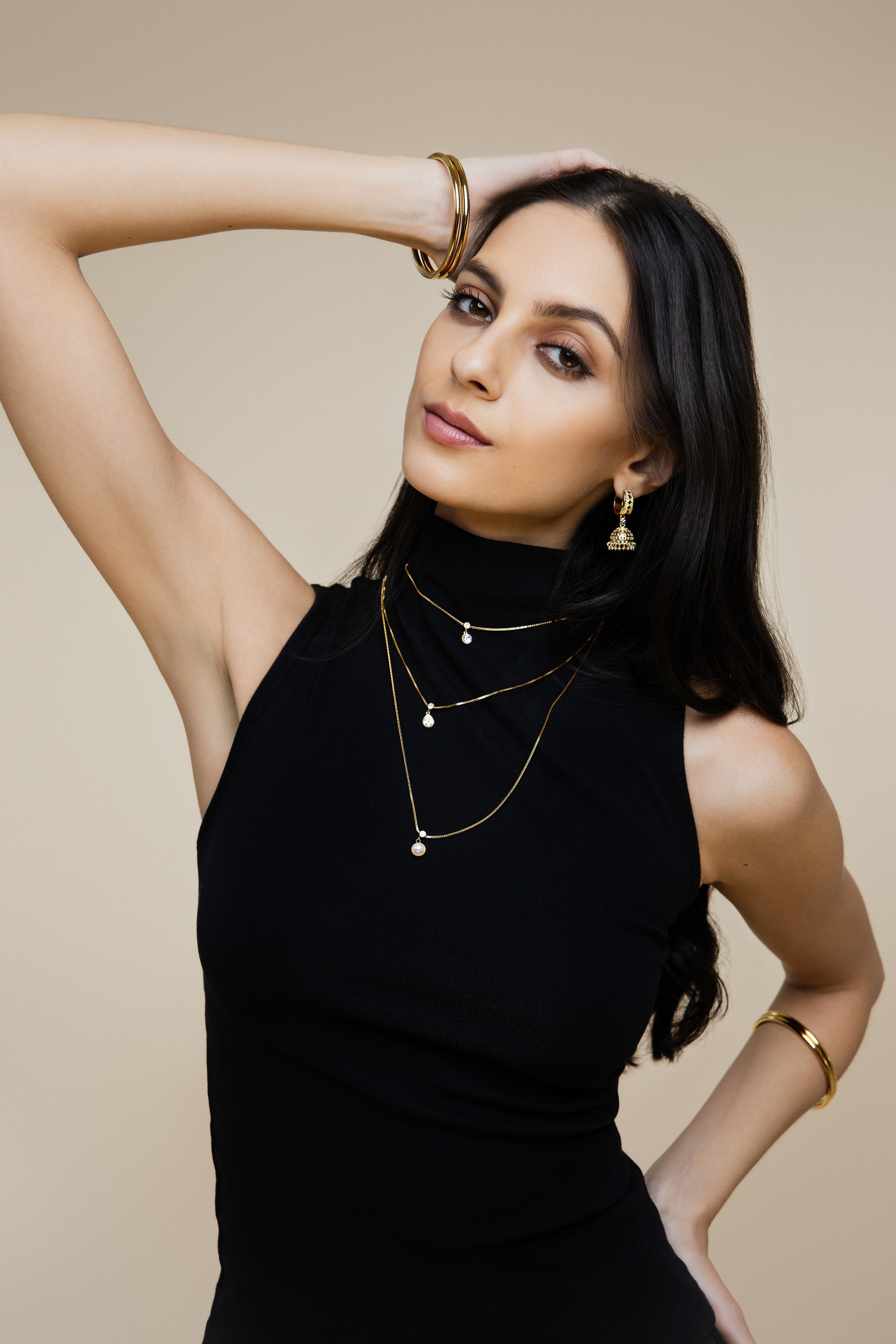 Woman wearing gold jewelry against a beige background