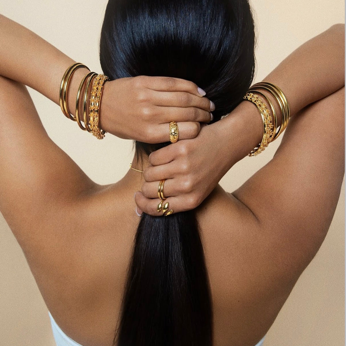 Person with long black hair and gold jewelry against a beige background